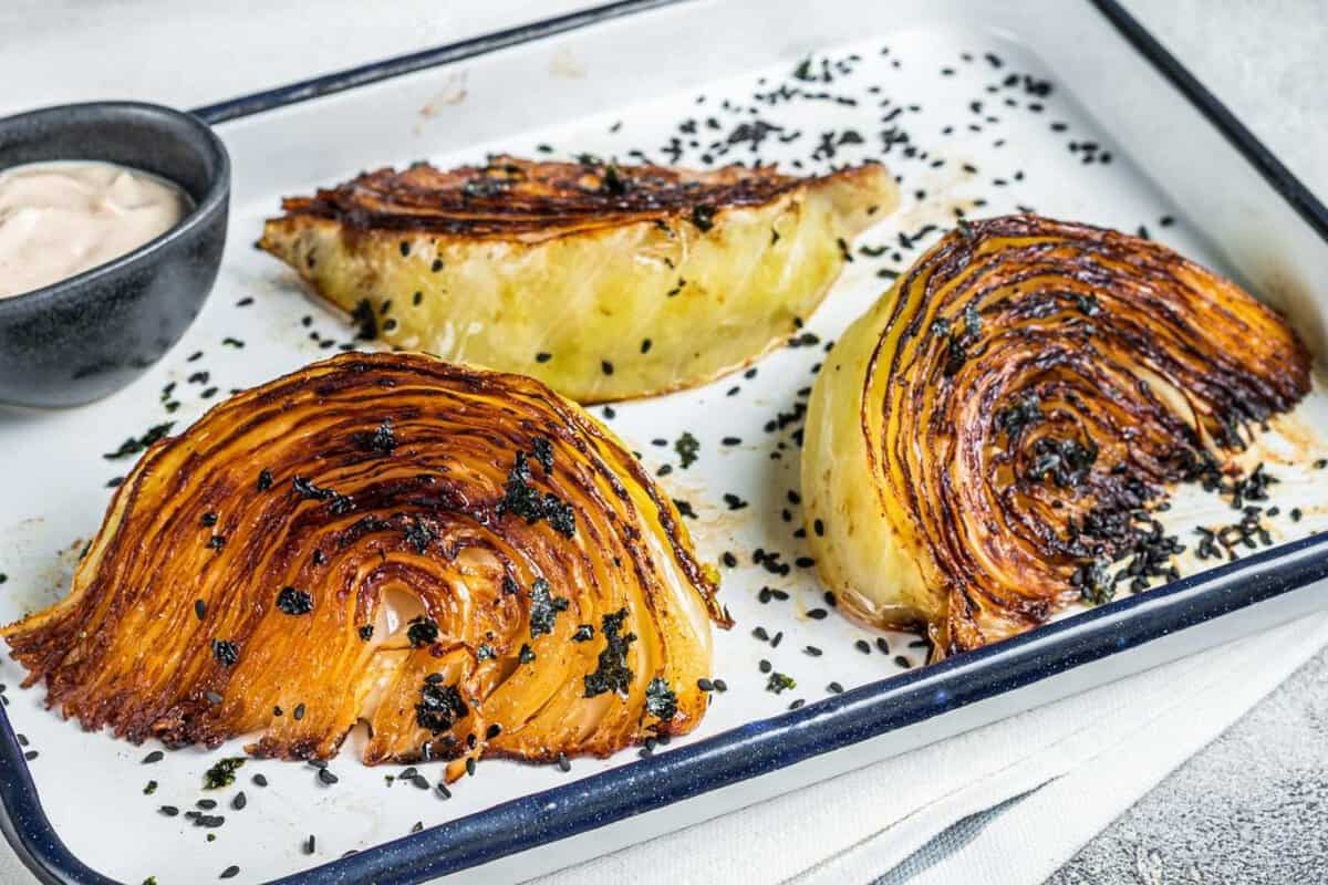 three roasted cabbage quarters and a small bowl of dressing in a baking sheet