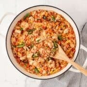 overhead view of finished rotisserie chicken and rice in a skillet with a wooden spoon about to serve