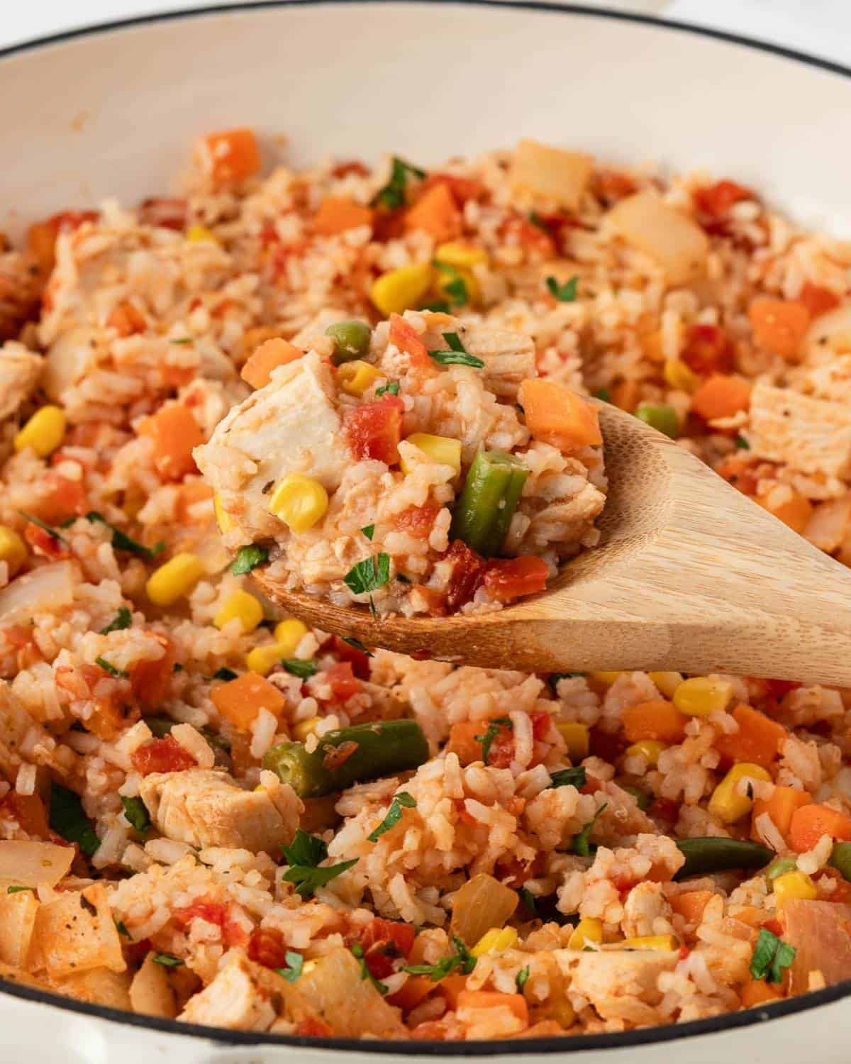 serving a chicken and rice recipe made with rotisserie chicken out of a skillet with a wooden spoon