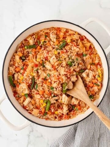overhead view of finished rotisserie chicken and rice in a skillet with a wooden spoon about to serve