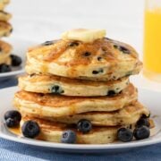 Stack of blueberry buttermilk pancakes on a plate topped with butter, syrup, and some blueberries on the plate