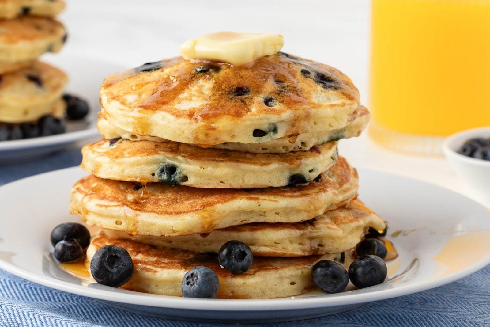 Stack of blueberry buttermilk pancakes on a plate topped with butter, syrup, and some blueberries on the plate