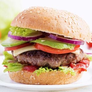a burger with lettuce, tomato, cheese, avocado, and onion