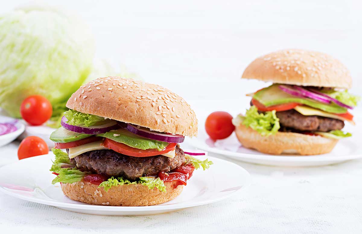 two burgers with lettuce, tomato, cheese, avocado, and onion