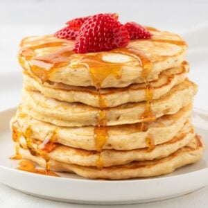 stack of protein pancakes on a plate, topped with sliced strawberries and a drizzle of syrup