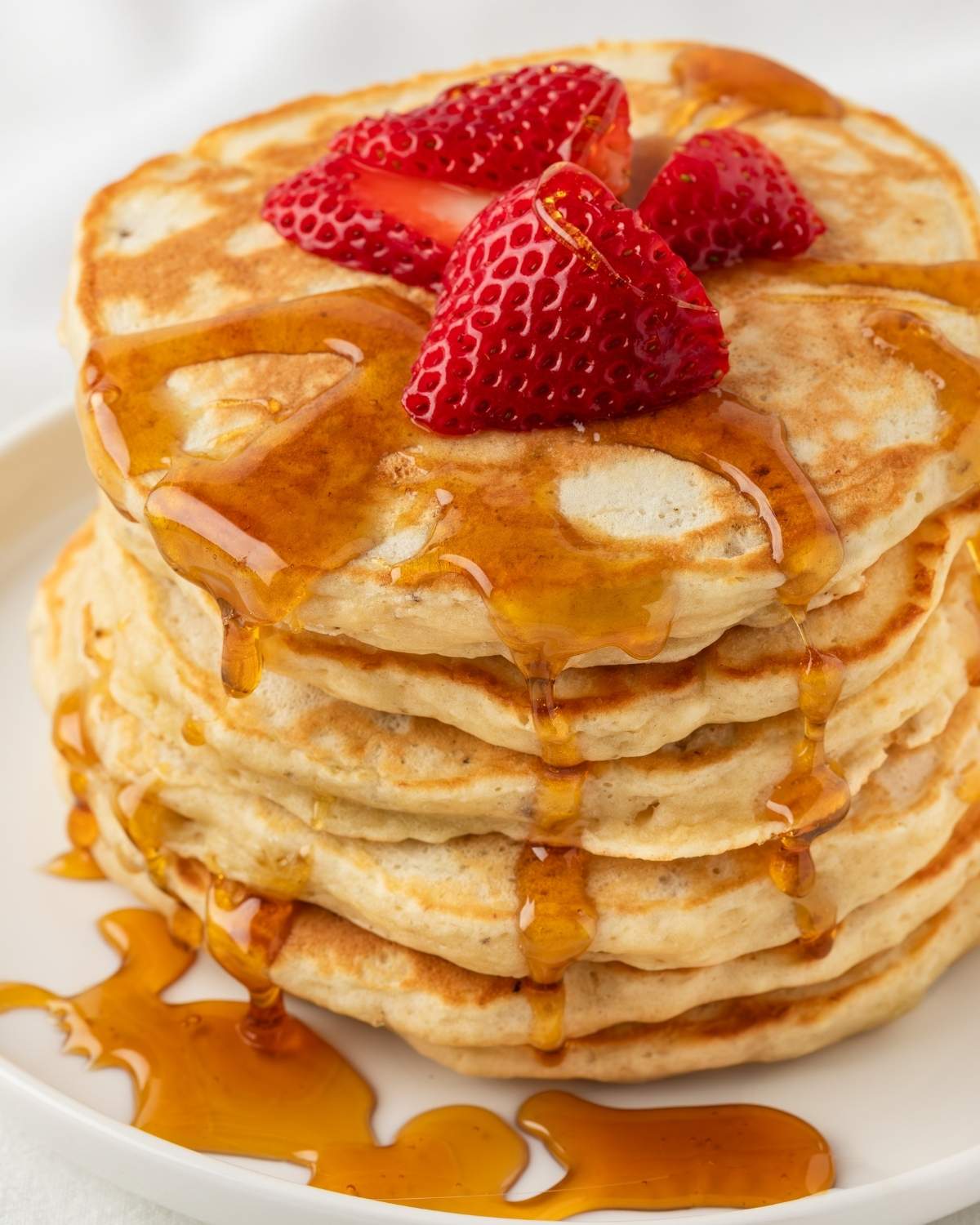 stack of protein pancakes on a plate, topped with sliced strawberries and a drizzle of syrup