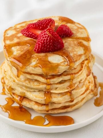 stack of protein pancakes on a plate, topped with sliced strawberries and a drizzle of syrup