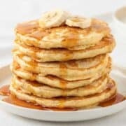 a stack of banana protein pancakes topped with banana slices and syrup