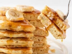 a fluffy stack of banana protein pancakes with a few pieces pierced through a fork