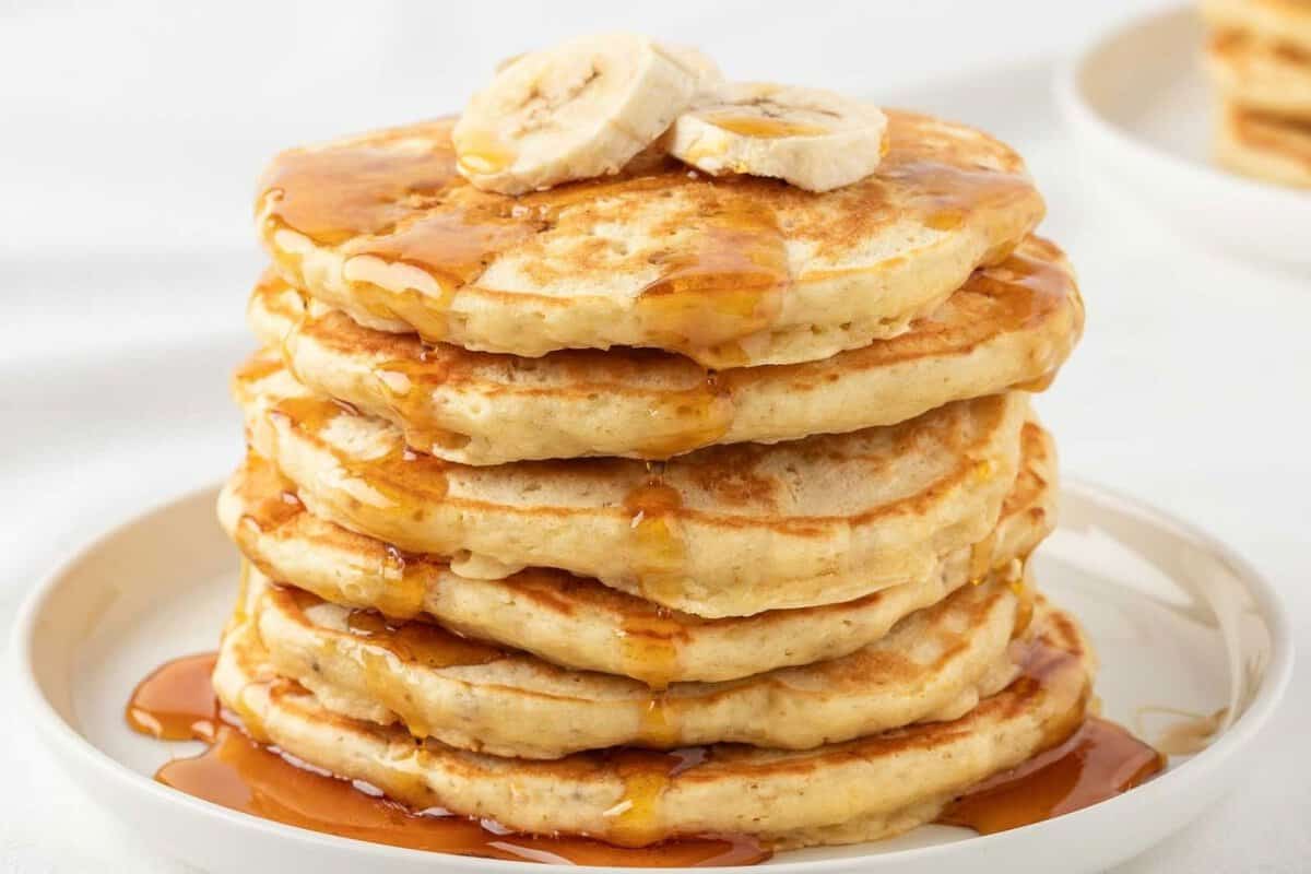 a stack of banana protein pancakes topped with banana slices and syrup