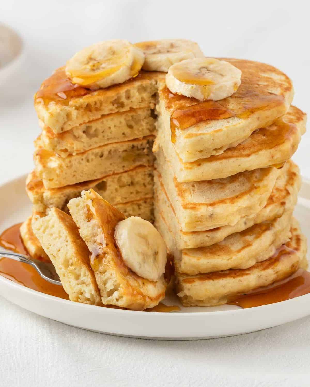 a fluffy stack of banana protein pancakes with a few pieces pierced through a fork