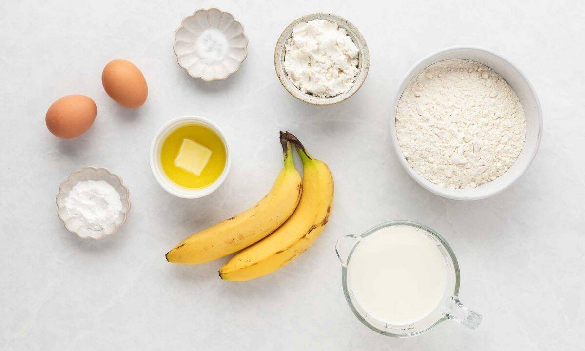 overhead view of pancake ingredients: eggs, butter, banana, flour, protein powder, milk, salt, and baking powder