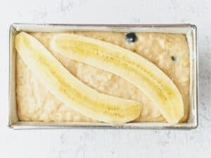 blueberry banana bread batter in a loaf pan topped with two banana slices
