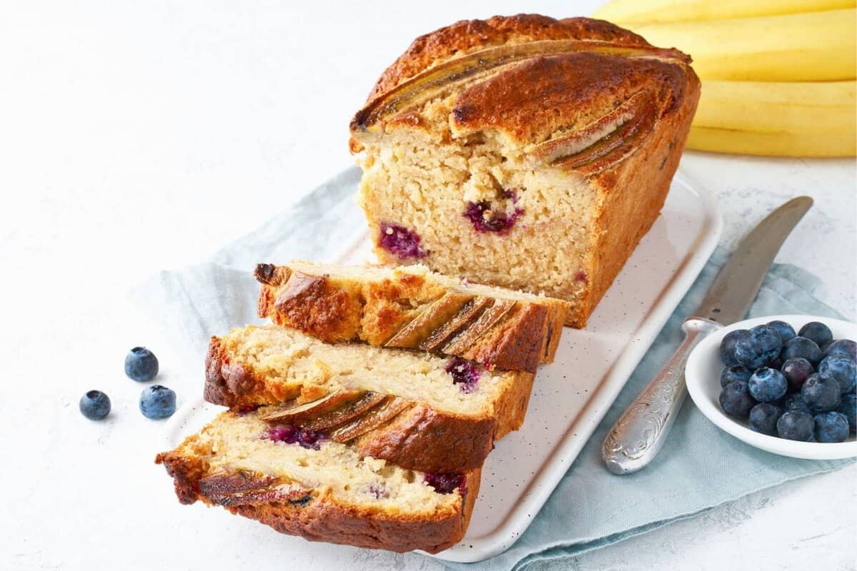 blueberry banana bread cut in slices on a tray and a little bowl of blueberries on the side