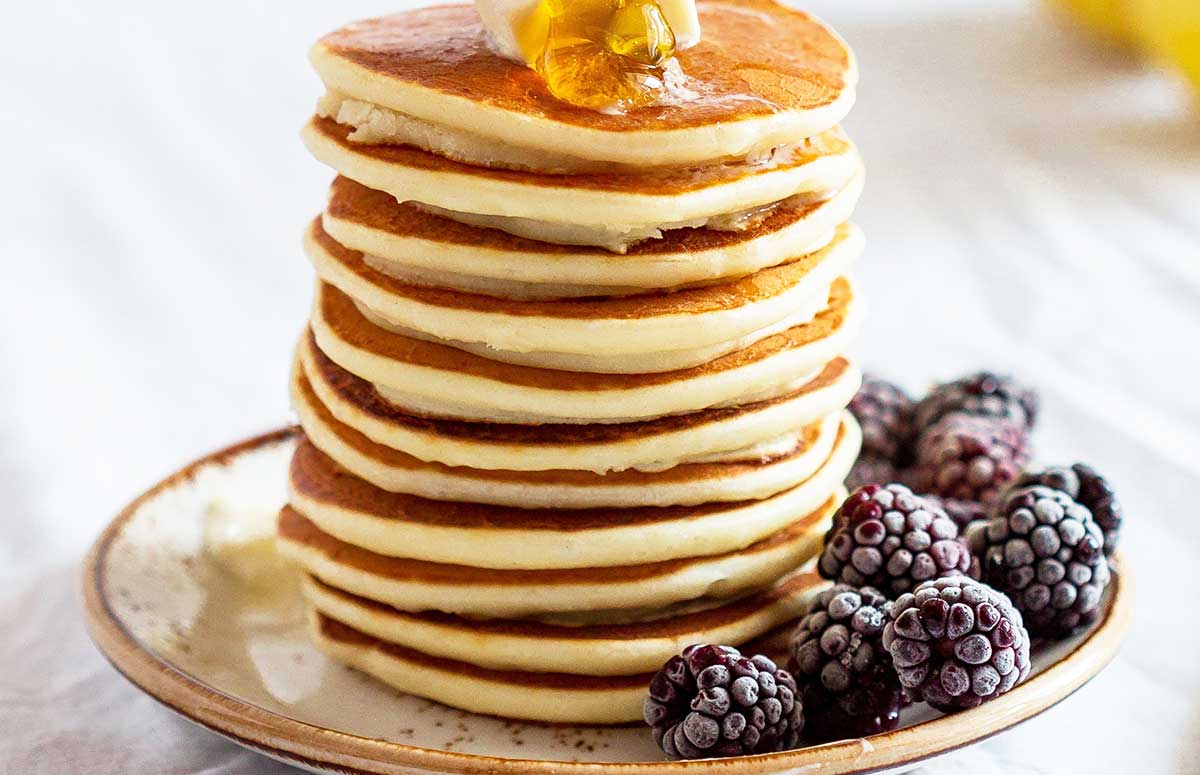 stack of pancakes made with protein powder on a plate with blackberries and butter on top