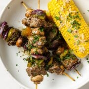 top view of a dish with 3 beef kabobs and a cob on the cob