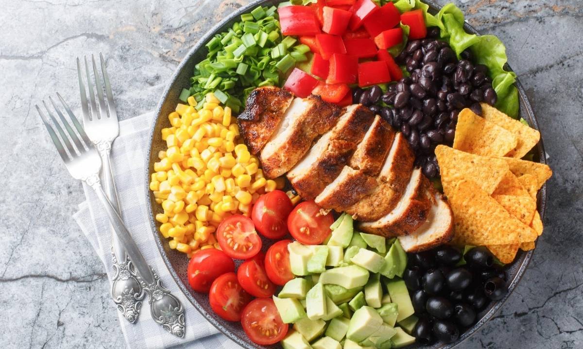 top view of a large bowl of Mexican salad made with corn, tomatoes, chicken, beans, avocado and chips