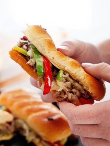 a person holding a philly cheesesteak skillet sandwich