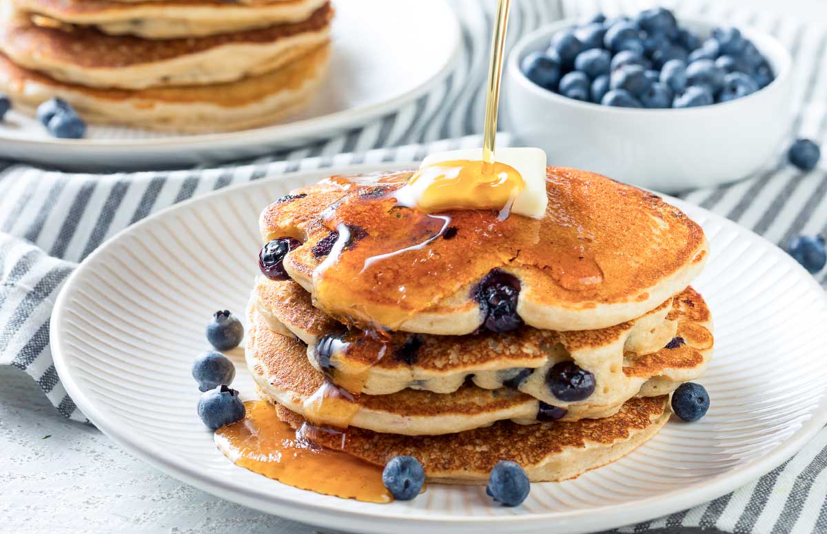 stack of blueberry pancakes with syrup being poured over them