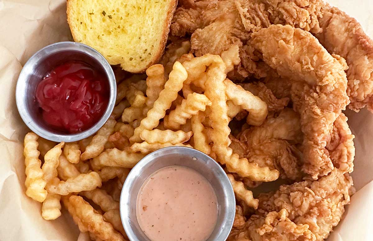 large plate of chicken tenders, crinkle french fries, Texas toast, and two dipping sauces