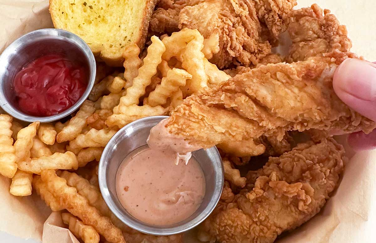copycat cane's chicken strips and french fries. one chicken strip dipping into a pin sauce