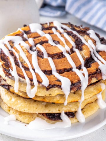 large stack of cinnamon roll pancakes topped with glaze