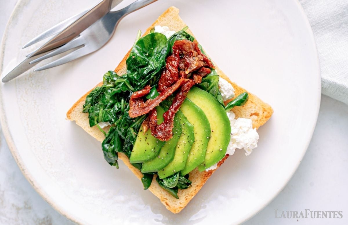 top view of a piece of toast with cottage cheese, avocado, spinach, and sun-dried tomatoes