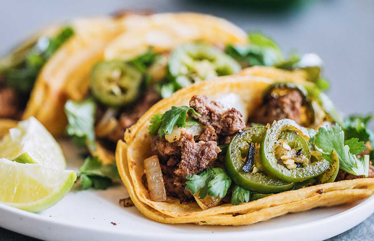 three ground chicken tacos on a dish with some lime wedges