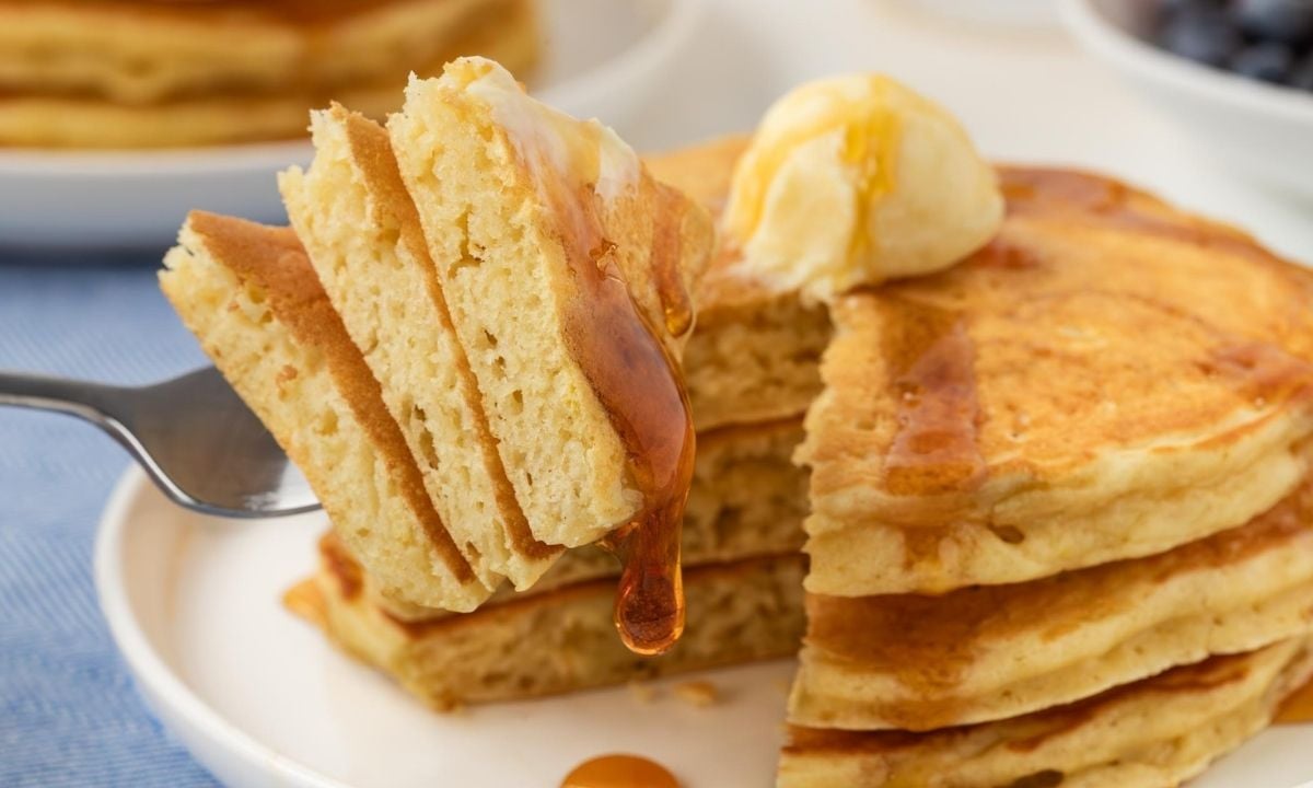stack of homemade IHOP pancakes on a white plate topped with butter and syrup with a closeup of a slice of pancakes on a fork to show fluffy texture