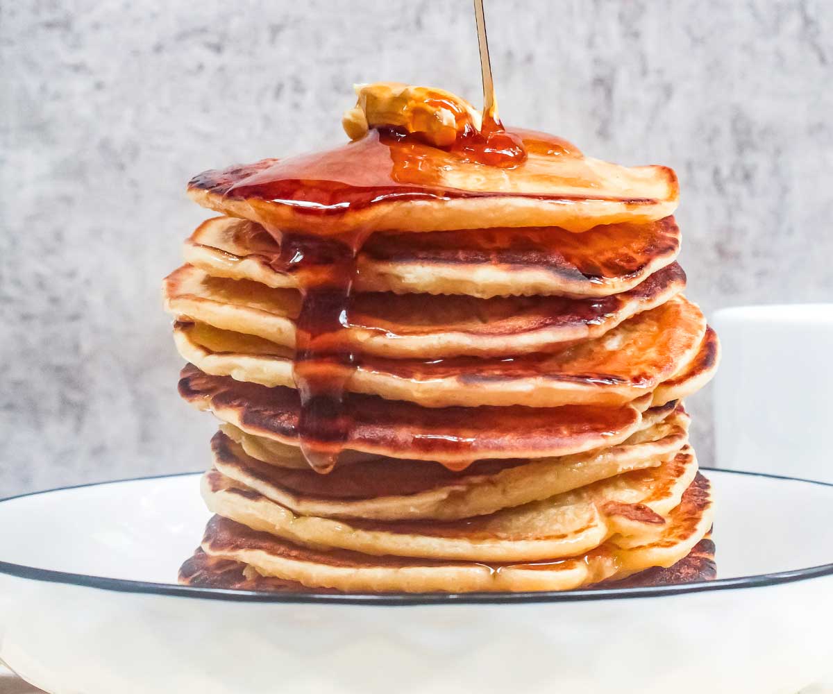 stack of pancakes on a white plate topped with syrup