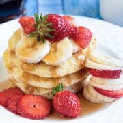 stack of three pancakes on a plate topped with sliced bananas and strawberries