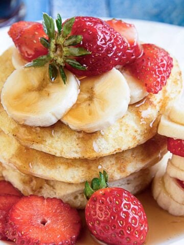 stack of strawberry banana pancakes on a plate with sliced bananas and strawberries