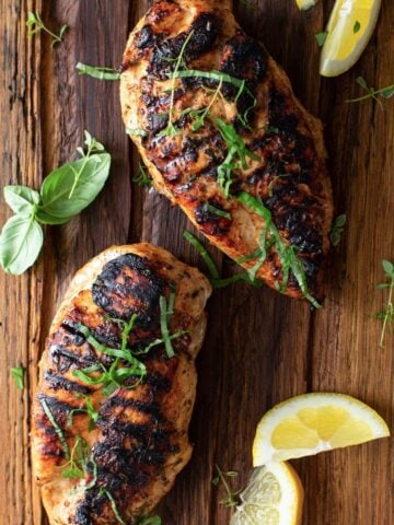 top view of two grilled chicken breasts and some lemon slices over a wooden table