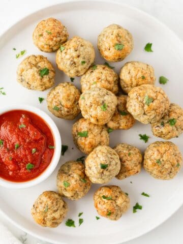 overhead view of baked chicken meatballs on a plate with marinara sauce in a small dish for dipping