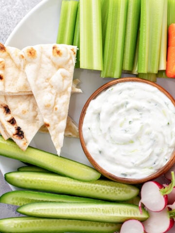 small bowl of a cottage cheese dip surrounded by celery, sliced radishes and pita