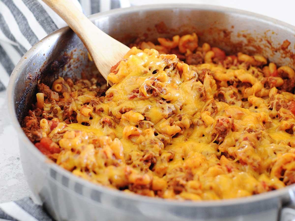 skillet of ground beef goulash topped with melted cheddar cheese