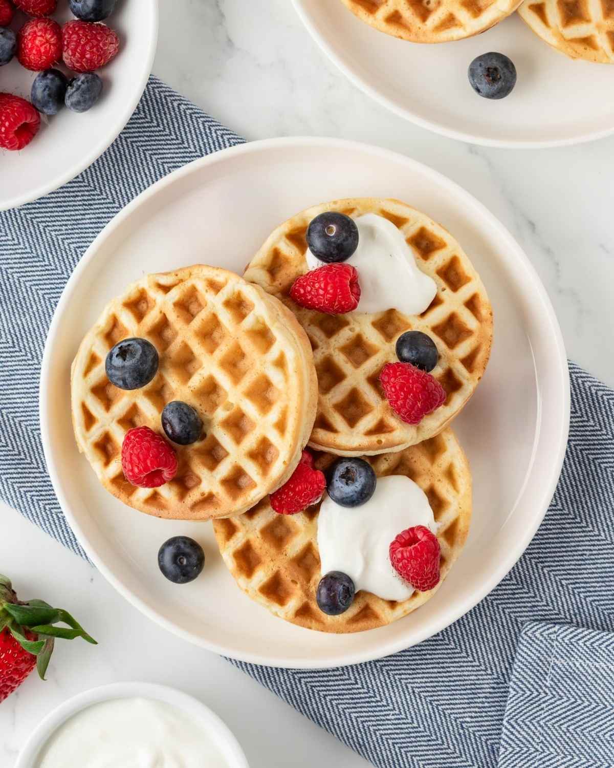3 protein powder waffles on a plate topped with a dollop of yogurt and fresh berries