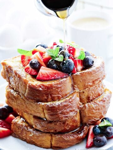 large stack of thick Texas toast French toast topped with berries and syrup being poured over the top