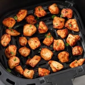 overhead view of cooked and seasoned chicken pieces in an air fryer