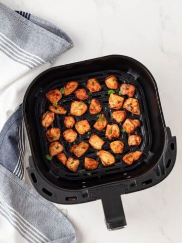 overhead view of cooked and seasoned chicken pieces in an air fryer