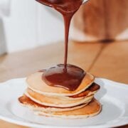 stack of pancakes with chocolate syrup being poured over the top
