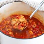 chicken goulash in a pot, with a ladle lifting tender chicken in a rich tomato-based broth