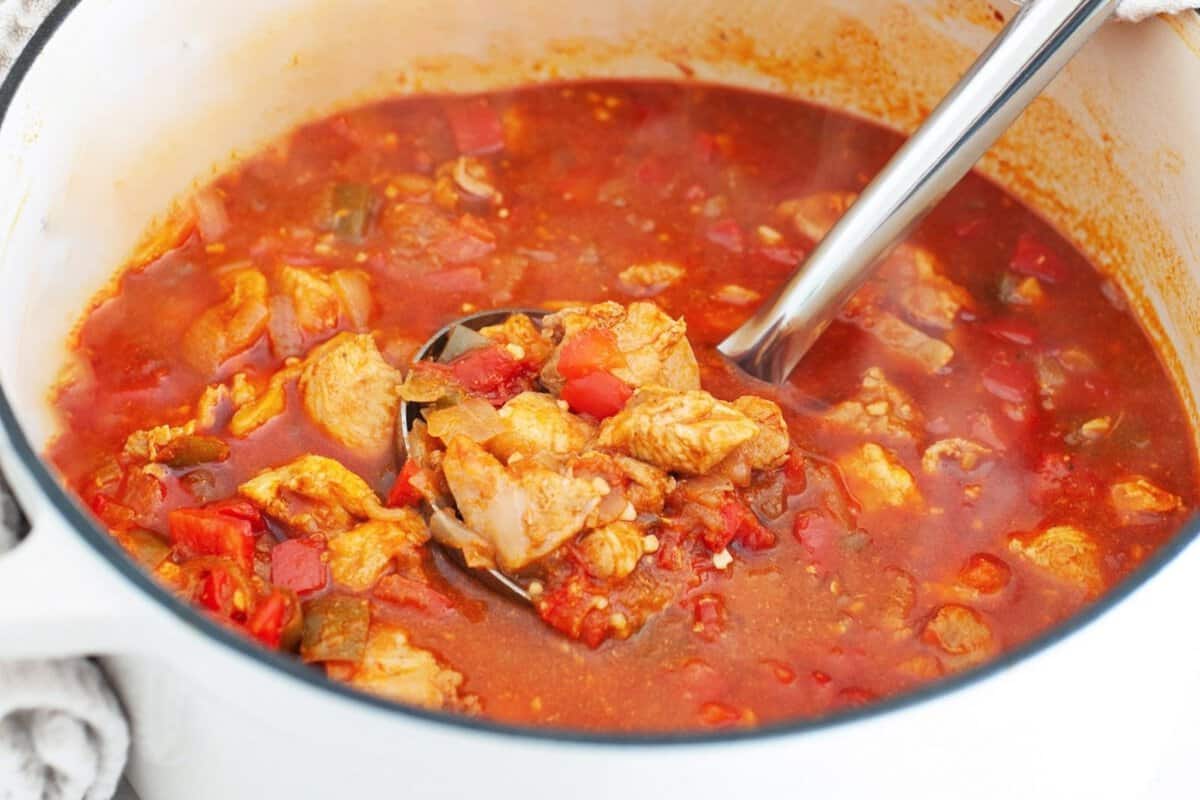 chicken goulash in a pot, with a ladle lifting tender chicken in a rich tomato-based broth