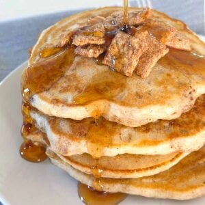 Stack of cinnamon toast crunch pancakes on a plate topped with more of the cereal with syrup on top