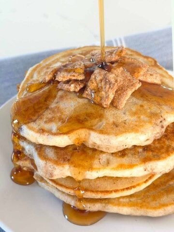Stack of cinnamon toast crunch pancakes on a plate topped with more of the cereal with syrup on top