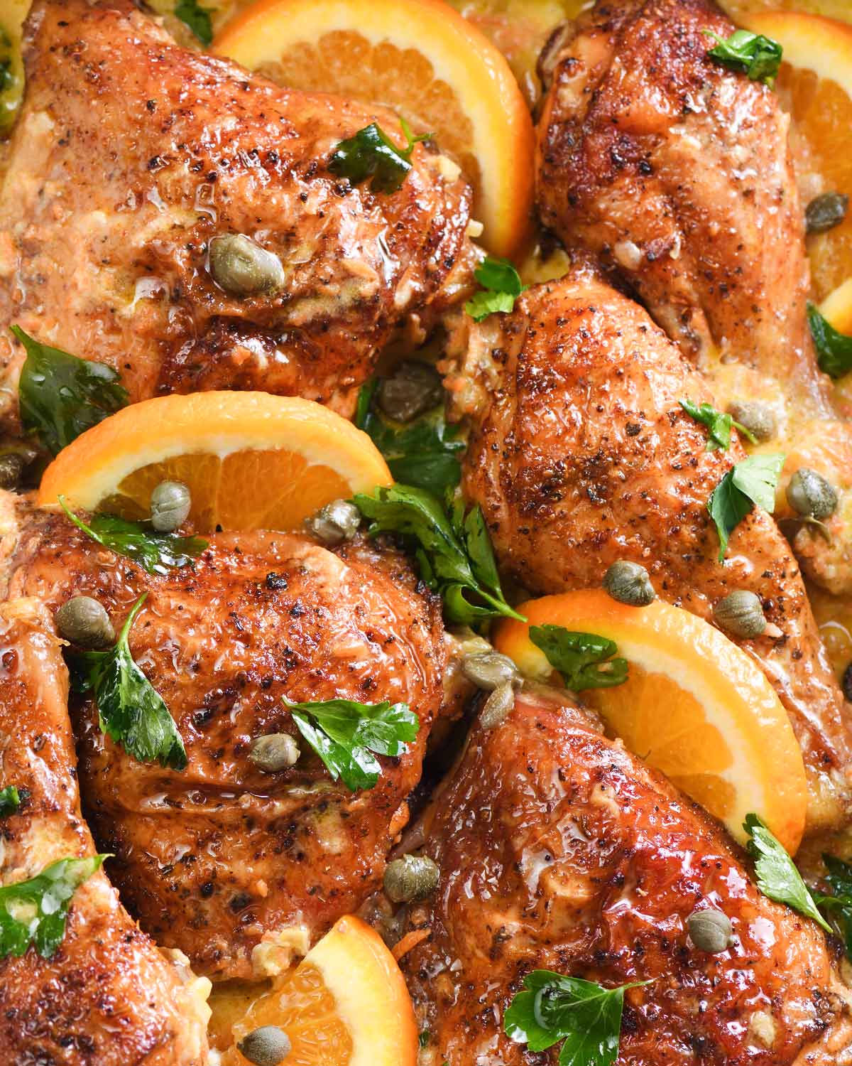 close up of chicken thighs with oranges in a baking dish