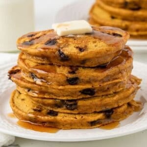 fluffy stack of pumpkin chocolate chip pancakes on a plate topped with butter and syrup