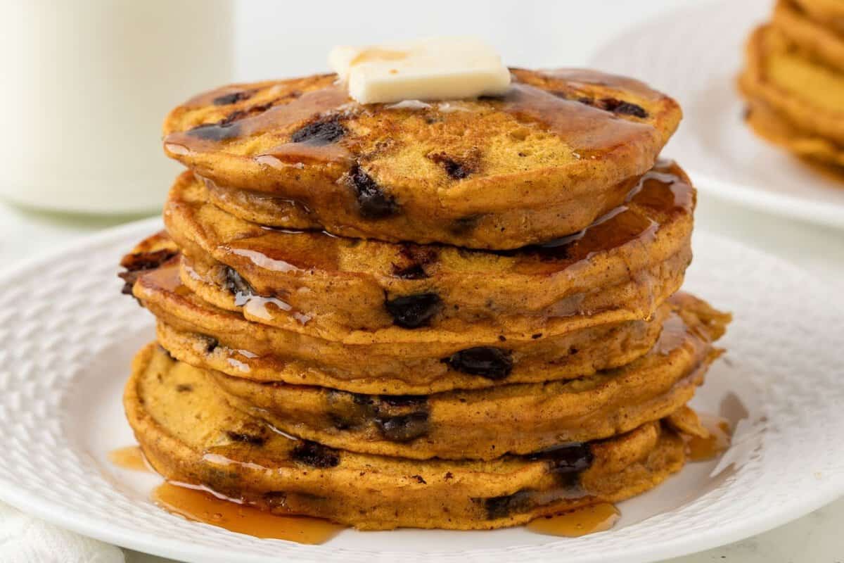 fluffy stack of pumpkin chocolate chip pancakes on a plate topped with butter and syrup