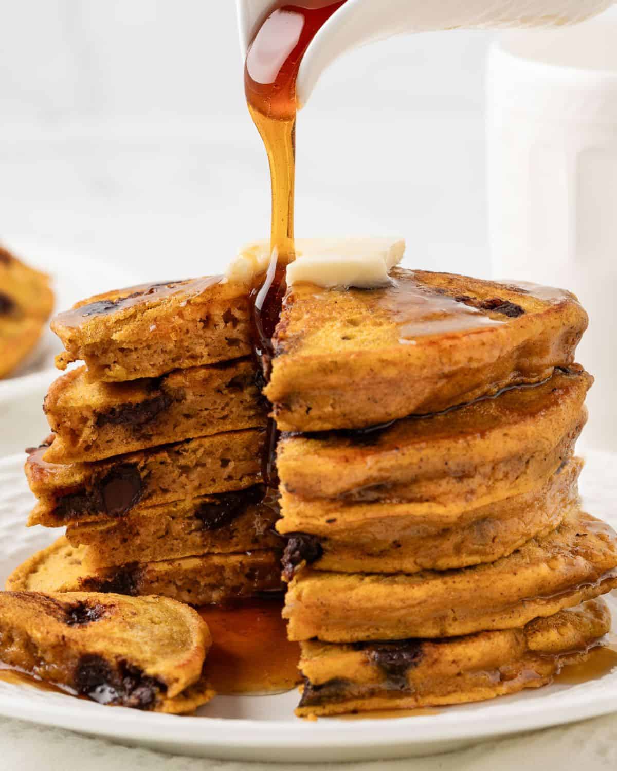 fluffy stack of pumpkin chocolate chip pancakes on a plate topped with butter and syrup, sliced to show the fluffy texture