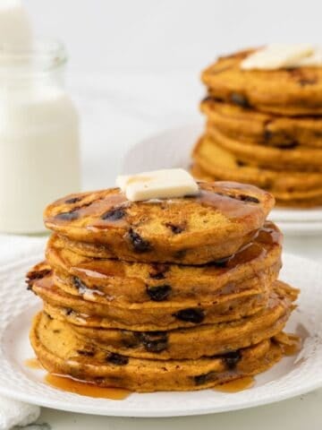 fluffy stack of pumpkin chocolate chip pancakes on a plate topped with butter and syrup